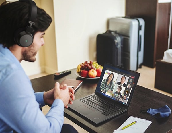 Un hombre con auriculares mirando hacia la derecha y hablando con otras personas visibles en la pantalla del portátil ThinkPad X13 de 4.ª generación